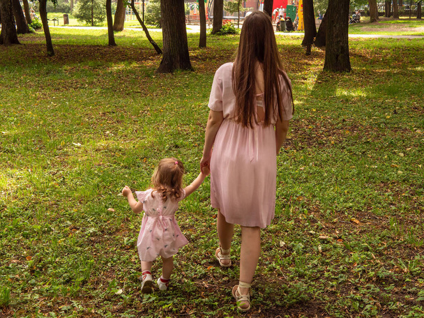 Mom and daughter walk and play in the park. Dressed in dresses. Sunny day, weekend in a city park. - Zdjęcie, obraz