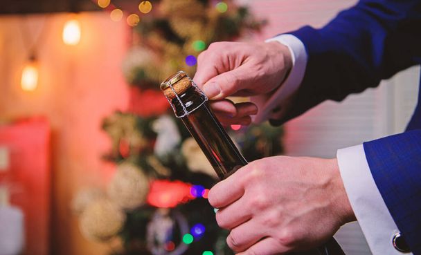Lets celebrate. Open champagne and celebrate holiday. Celebrate new year with champagne drink. Toast and cheers concept. Male hands opening champagne bottle on christmas decorations background - Photo, Image