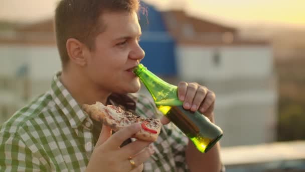 Chłopak pije piwo i je pizzę na imprezie. - Materiał filmowy, wideo