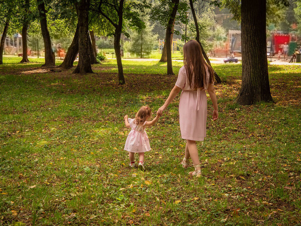 Mom and daughter walk and play in the park. Dressed in dresses. Sunny day, weekend in a city park. - Photo, Image