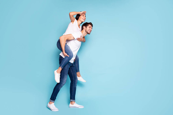 Full length body size profile side view of nice attractive cheerful dreamy couple piggybacking having fun looking watching vacation isolated on bright vivid shine vibrant blue turquoise background - Fotoğraf, Görsel