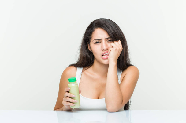 Молода іспаномовна жінка тримає овочевий напій кусає нігті, нервує і дуже тривожно
. - Фото, зображення