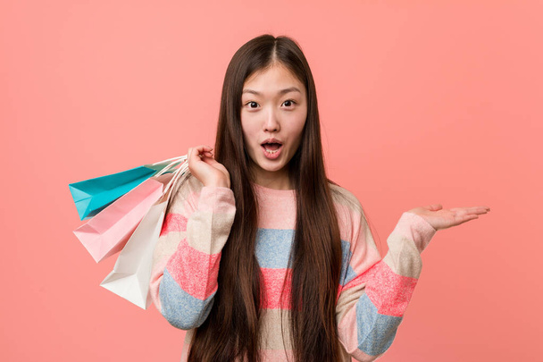 młoda Azji kobieta trzyma a zakupy torba pod wrażeniem trzymając kopia przestrzeń na dłoni. - Zdjęcie, obraz