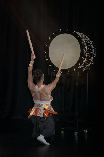 Taiko baterista golpea el tambor grande en el escenario sobre un fondo negro, vista trasera
. - Foto, imagen