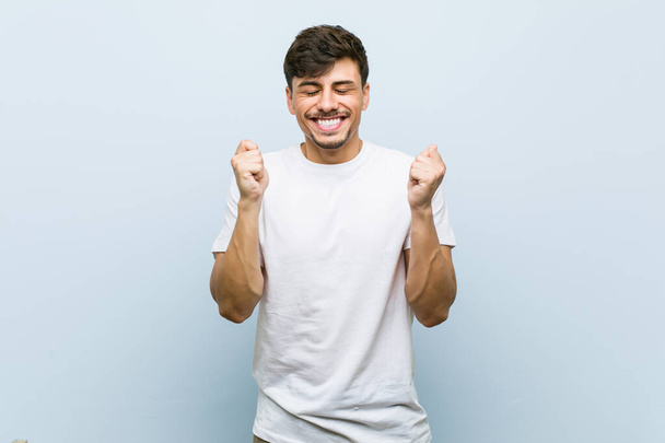 Giovane uomo caucasico indossa una maglietta bianca alzando il pugno, sentendosi felice e di successo. Concetto di vittoria
. - Foto, immagini