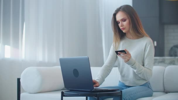 Nuori kaunis blondi nainen katsoo kannettavan tietokoneen näyttöä ja pitää pankkikorttia käsissään. Pankkipalvelujen etäkäyttö Internetin kautta
 - Materiaali, video