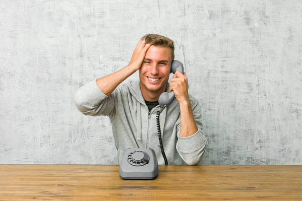 Young man talking on a vintage phone laughs joyfully keeping hands on head. Happiness concept. - Photo, Image