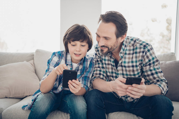 Younger generation and digital devices gadgets concept. Photo of smart clever understands how to use modern technology shows screen of his telephone to daddy sitting on comfort divan - 写真・画像