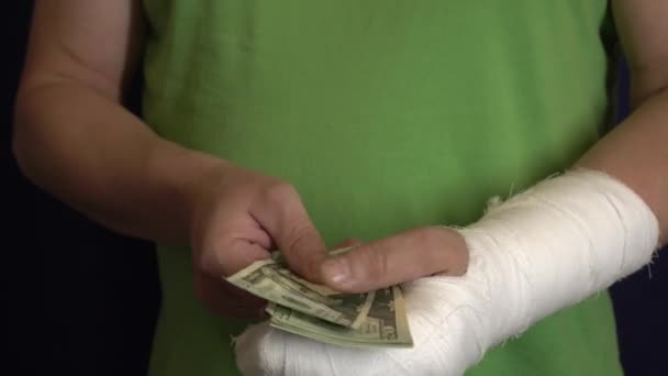 ein Mann mit einem Gips hält Geld von den Kosten und Ausgaben für die medizinische Notfallversorgung in einem Krankenhaus fern . - Filmmaterial, Video
