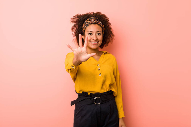 Nuori afrikkalainen amerikkalainen nainen vaaleanpunaista taustaa vasten hymyilevä iloinen näyttely numero viisi sormin
. - Valokuva, kuva