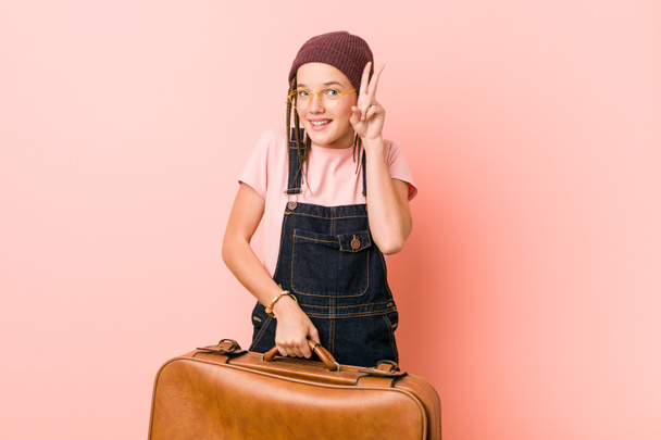 Young caucasian woman holding a suitcase showing victory sign and smiling broadly. - Zdjęcie, obraz