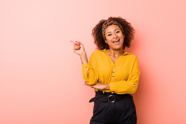 Young african american woman against a pink background smiling cheerfully pointing with forefinger away. - Photo, Image