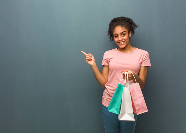 Young black woman smiling and pointing to the side. She is holding a shopping bags. - Photo, Image