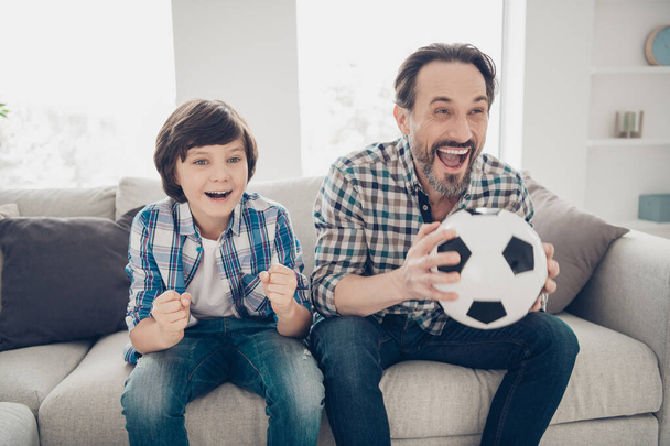 Portrait of two nice attractive lovely cute cheerful cheery overjoyed guys dad and pre-teen son sitting on sofa watching sport show online in light white modern style interior house living-room - Fotó, kép