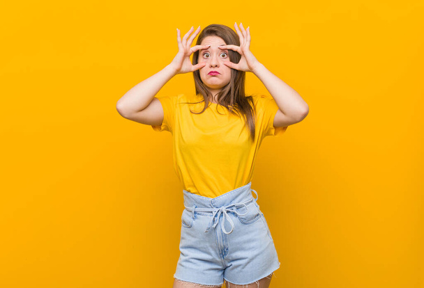 Young woman teenager wearing a yellow shirt keeping eyes opened to find a success opportunity. - 写真・画像