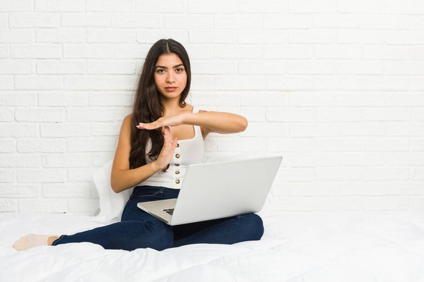 Jovem árabe mulher trabalhando com seu laptop na cama mostrando um gesto timeout
. - Foto, Imagem
