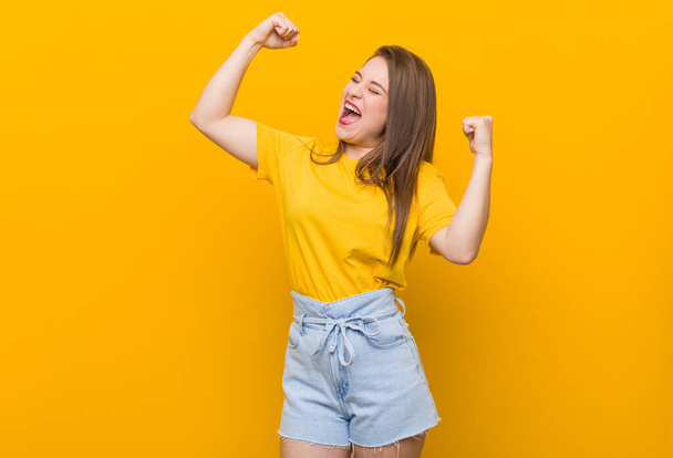 Giovane donna adolescente indossa una camicia gialla alzando il pugno dopo una vittoria, concetto vincitore
. - Foto, immagini