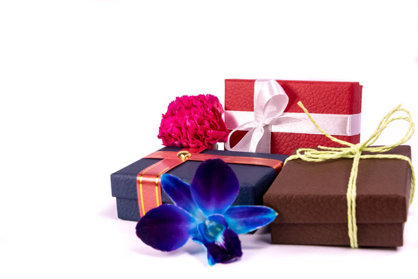 Три подарочных коробки с красивыми лентами и нитями, голубые цветы орхидеи и розовая гвоздика на белом фоне для копирования пространства
 - Фото, изображение
