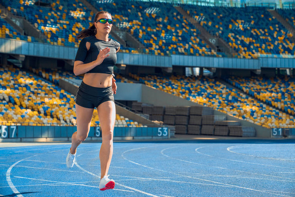 Female athlete sprinting on a running track in a stadium. - Fotó, kép