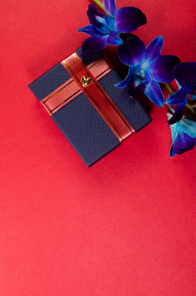 Top kilátás kék ajándék doboz díszített szalag és kék orchidea virág piros háttér romantikus ajándékok koncepció másolási hely - Fotó, kép