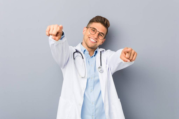 Young blonde doctor man cheerful smiles pointing to front. - Photo, Image