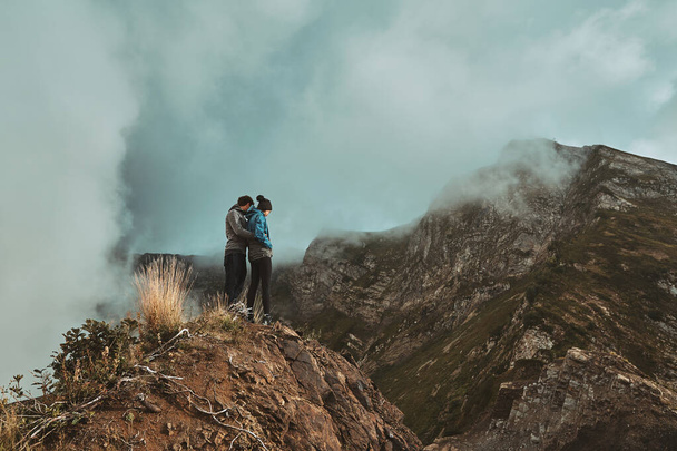 a young couple standing on a cliff in the mountains looking down - Photo, Image