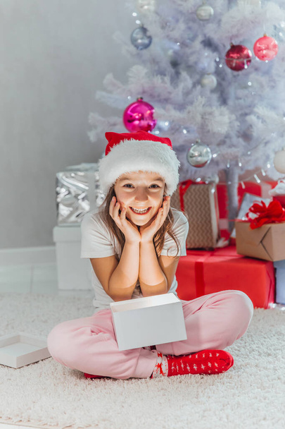 Fijne feestdagen Leuke kleine kinderopeningscadeau bij de kerstboom. Het meisje dat lacht en geniet van het geschenk. - Foto, afbeelding