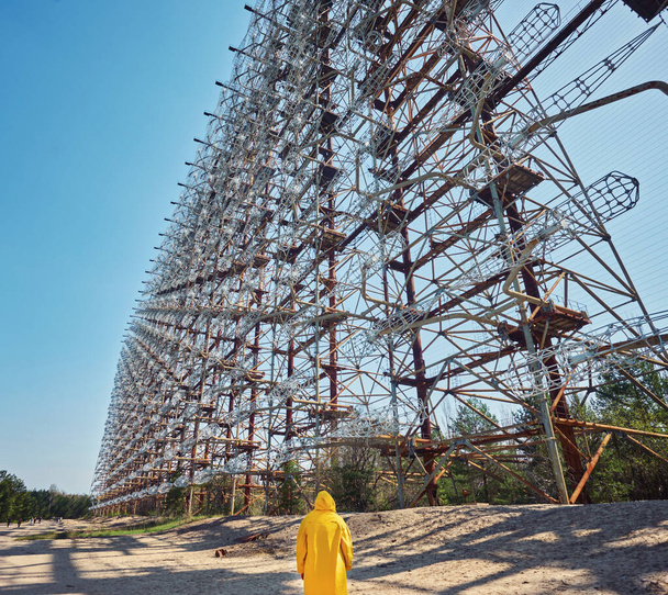 Молодий чоловік у жовтому захисному костюмі, що стоїть біля військового секретного радара "Дуга" в Чорнобилі (Україна). - Фото, зображення