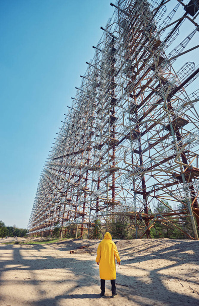 jovem em terno protetor amarelo que está perto de radar de antena de objeto secreto militar Duga em Chernobyl, na Ucrânia
 - Foto, Imagem