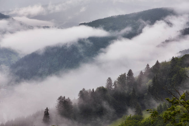 雨上がりに霧の海に浸かる尾根を背景に、西ヨーロッパの山岳地帯や高山の村 - 写真・画像
