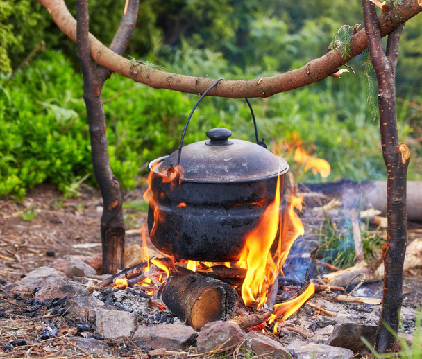 alter kleiner Wasserkocher wird bei schlechtem Wetter am Lagerfeuer auf einer grünen Bergwiese angeheizt. - Foto, Bild