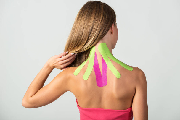 Woman shows kinesio tapes taped to her neck. Isolated on white background. Alternative medicine concept - Фото, изображение