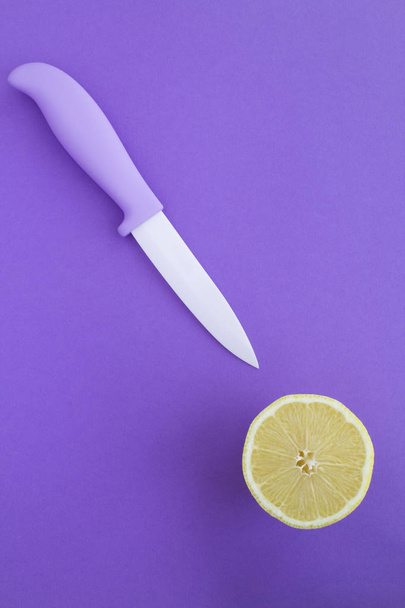 Cuchillo violeta y medio limón sobre fondo violeta. Vista superior. Copiar espacio. Ubicación vertical
. - Foto, Imagen