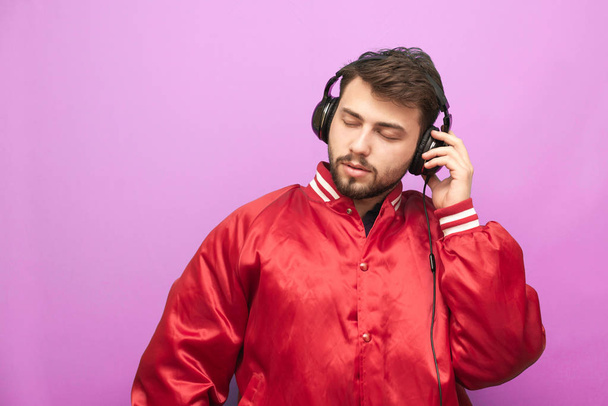 Κοντινό πλάνο πορτρέτο ενός ενήλικου άνδρα ακούει μουσική σε ακουστικά με κλειστά μάτια σε ροζ φόντο. Ο μουσικός ενθουσιώδης απολαμβάνει τη μουσική. Μεμονωμένα - Φωτογραφία, εικόνα