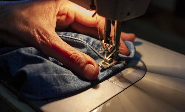 As mãos femininas em uma velha máquina de costura cosem a ganga. Close-up
 - Foto, Imagem
