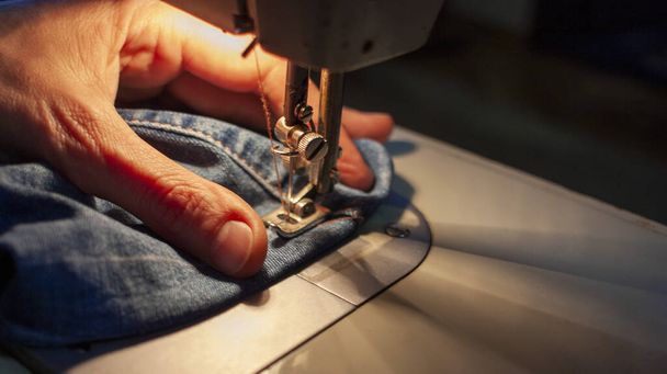 Las manos femeninas en una vieja máquina de coser cosen denim. Primer plano
 - Foto, Imagen