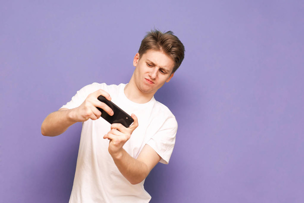 Disgruntled guy playing the game on a smartphone, focused lookin - 写真・画像