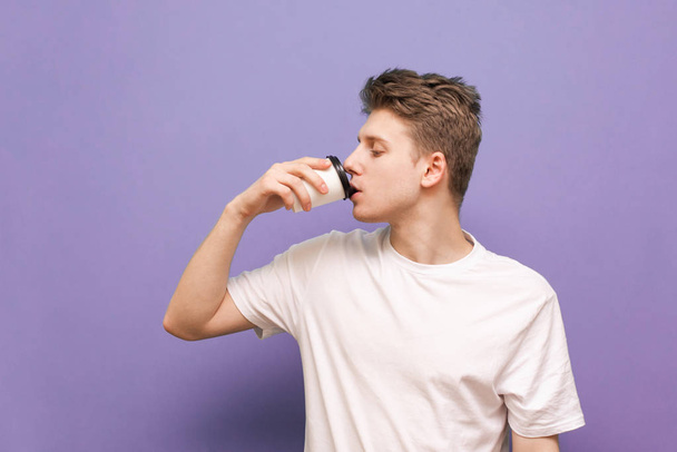 Hombre joven en una camiseta blanca bebiendo café de una taza de papel en
 - Foto, Imagen
