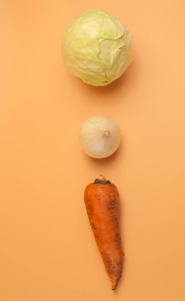 organic carrots,onions and cabbage on beige background,unpeeled sweet carrots,onions and cabbage for soup, minimalist style vegetables from the garden,vitamins,vegetarian food,healthy eating concept. - Photo, image