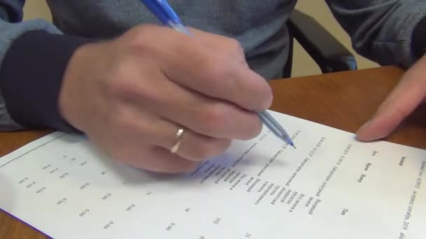 ελέγχοντας ένα τελειωμένο έγγραφο και διαβάζοντάς το, ένας άνθρωπος κάνει διορθώσεις στις καταχωρήσεις σε ένα φύλλο λευκού χαρτιού με ένα στυλό μπλε μελάνης, κοντινό πλάνο - Πλάνα, βίντεο