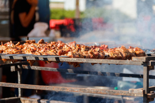 Grilled kebab cooking on metal skewer. Roasted meat cooked at barbecue.Traditional eastern dish, shish kebab. Grill on charcoal and flame, picnic, street food - Photo, Image