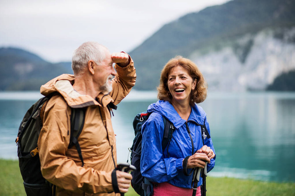 A senior pensioner couple hiking by lake in nature, talking. - Fotoğraf, Görsel