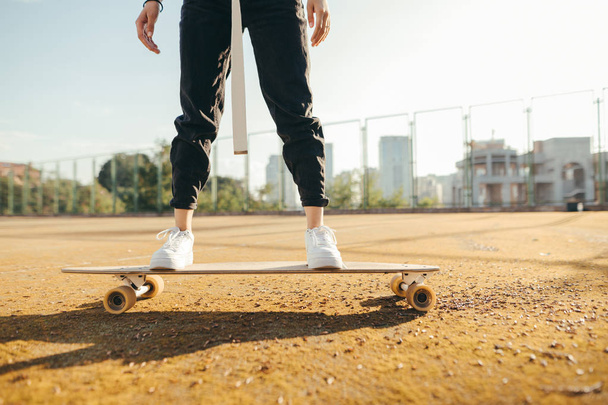 Foto aus nächster Nähe, Mädchen in stylischen Klamotten und Turnschuhen fahren auf einem Longboard. Die Füße des Mädchens stehen auf einem Skateboard. Hintergrund. Nahaufnahme - Foto, Bild