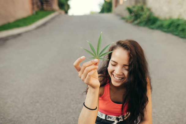 Chica sonriente sostiene en su mano una hoja de cáñamo en el año y sonríe. Concepto de drogas fáciles
. - Foto, imagen