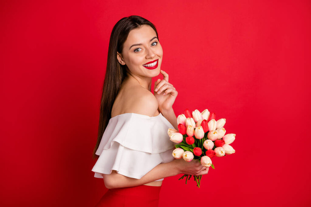 Portrait of gorgeous lady holding fresh flowers touching teeth wearing off-shoulders top isolated over red background - Fotoğraf, Görsel