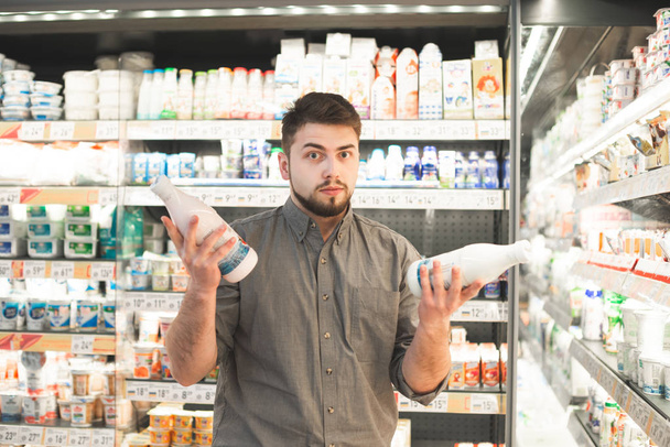 Мужчина стоит с двумя бутылками молока в молочном отделе
  - Фото, изображение