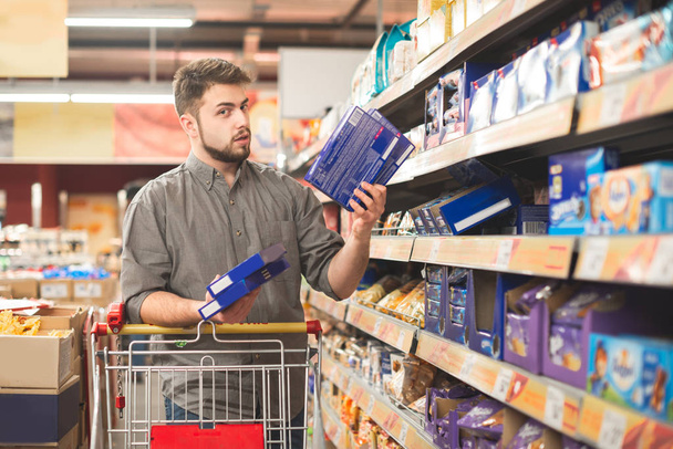 Portret mężczyzny w średnim wieku mylić robi zakupy w supermarkecie: wywołanie jego żona pyta jaki deser, wybrać - Zdjęcie, obraz