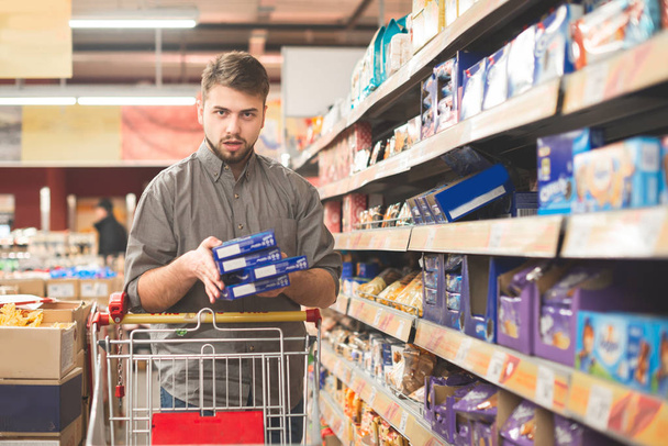 Man with a bundle of cookies in the hands and shopping cart in a - Foto, Bild