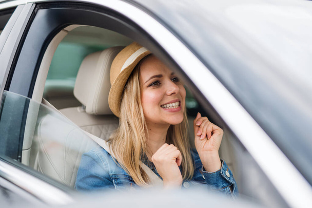 Young woman with hat sitting in car, listening to music and dancing. - Foto, imagen