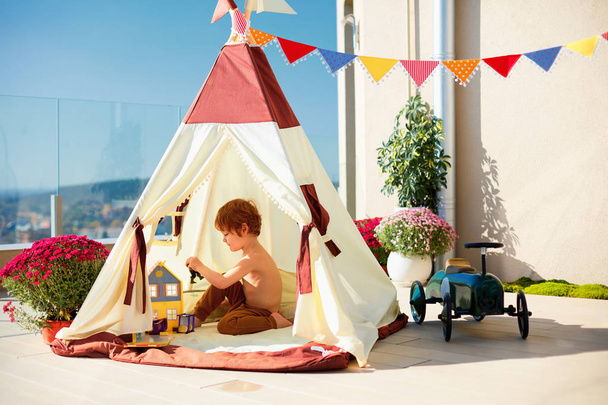 cute toddler kid, boy playing peacefully inside of a teepee tent on sunny rooftop patio - 写真・画像